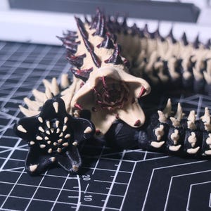 May include: A black, five-pointed star-shaped figure with white dots, next to a detailed, beige and black creature with a spiky back and a large, open-mouthed head. The objects are on a black grid.