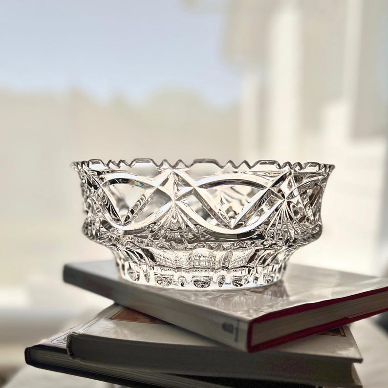 Peut inclure: Un bol en verre taill&eacute; transparent avec un motif d&eacute;taill&eacute; de diamants et d'&eacute;clats d'&eacute;toiles. Le bol a un bord festonn&eacute; et repose sur une pile de livres. Le verre refl&egrave;te la lumi&egrave;re, cr&eacute;ant un effet scintillant. Une pi&egrave;ce d&eacute;corative pour servir ou exposer.