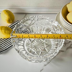 Peut inclure: Un bol en verre taill&eacute; transparent avec un motif en &eacute;toile au centre, mesurant environ 20 cm de diam&egrave;tre. Le bol a un bord festonn&eacute; et est pos&eacute; sur une surface en marbre. Deux citrons et un tissu &agrave; rayures noires et blanches sont visibles.