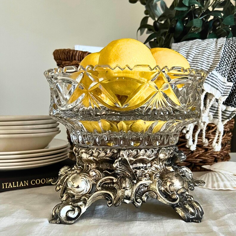 Peut inclure: Un saladier en verre taill&eacute; transparent rempli de citrons jaunes, pos&eacute; sur un support en m&eacute;tal argent&eacute; orn&eacute;. Le saladier pr&eacute;sente un motif en losange. Le support a un design d&eacute;taill&eacute; en volutes. Un centre de table d&eacute;coratif.