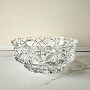 Peut inclure: Un bol en verre taill&eacute; transparent avec un motif g&eacute;om&eacute;trique d&eacute;taill&eacute;. Le bol a une forme large et peu profonde avec un bord festonn&eacute; et une base en pi&eacute;destal. Le design complexe refl&egrave;te la lumi&egrave;re.