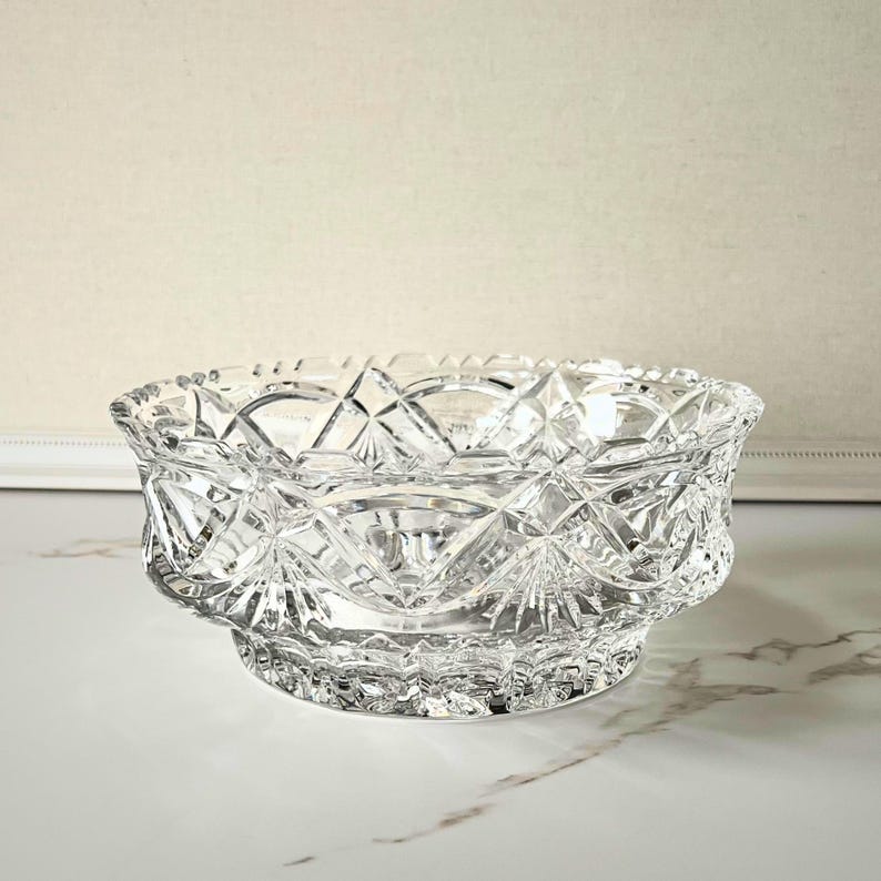Peut inclure: Un bol en verre taill&eacute; transparent avec un motif g&eacute;om&eacute;trique d&eacute;taill&eacute;. Le bol a une forme large et peu profonde avec un bord festonn&eacute; et une base en pi&eacute;destal. Le design complexe refl&egrave;te la lumi&egrave;re.