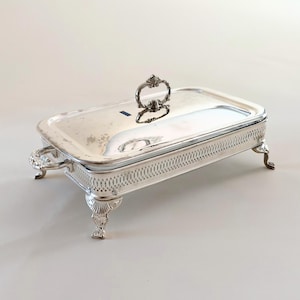 May include: A rectangular silver-plated serving dish with a removable lid featuring a central handle. The base has an intricate pierced lattice pattern along the sides, four ornate cabriole legs, and two side handles for easy transport.