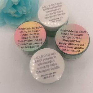 May include: Four small round containers of handmade lip balm with white lids and colourful labels. The labels list ingredients including white beeswax, mango butter, shea butter, sweet almond oil, and cinnamon vanilla essential oil, with 28g net weight.