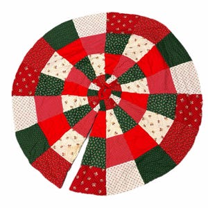 May include: A round, patchwork Christmas tree skirt with a vibrant design. The skirt features a radial pattern of red, green, white, and cream-colored fabric squares. The fabric has floral and polka dot patterns.