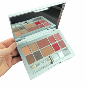 Op de afbeelding: Zilveren make-uppalet met een ingebouwde spiegel, met verschillende tinten oogschaduw, blush en lipkleur. Inclusief twee applicatorborstels. Het palet is opengeklapt en toont de reeks kleuren.