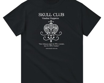 May include: Black t-shirt with white graphic text and design. The text reads "SKULL CLUB Voodoo Happens." Below the graphic is the text "New Orleans might be 90% Catholic, but it's 100% Voodoo." and the website address.