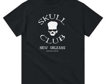May include: Black t-shirt with a white graphic featuring a skull design and the words "SKULL CLUB" above and "CLUB" below the skull. The text "NEW ORLEANS" and website address are below the club name.