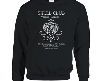 May include: Black sweatshirt with white text and graphic. The text reads "SKULL CLUB Voodoo Happens" above a stylized heart design. Below the graphic is the text "New Orleans might be 90% Catholic, but it's 100% Voodoo." and the website address.