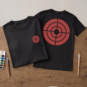 Puede incluir: Dos camisetas negras con un diseño de diana roja. Una camiseta muestra una diana pequeña en el pecho izquierdo, mientras que la otra presenta una diana roja grande y prominente centrada en la parte posterior. Ambas tienen mangas cortas.