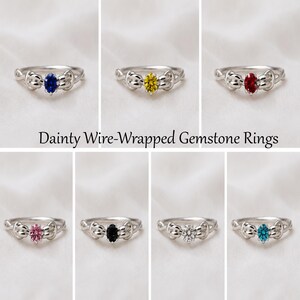 Peut inclure: Plusieurs bagues en argent filaire, chacune ornée d'une pierre précieuse ovale de couleur différente. Les pierres sont bleues, jaunes, rouges, roses, noires, transparentes et turquoise. Le texte "Dainty Wire-Wrapped Gemstone Rings" est affiché.