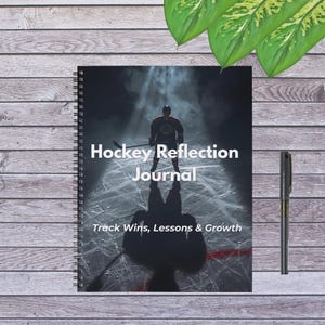May include: A spiral-bound notebook titled "Hockey Reflection Journal" with a hockey player image on the cover. The cover also includes the text "Track Wins, Lessons & Growth." A pen rests beside the notebook on a wooden surface.