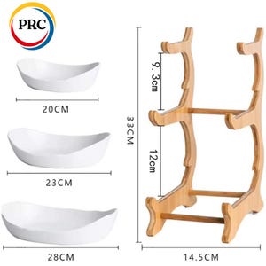 May include: Three white oval ceramic bowls measuring 20 cm, 23 cm, and 28 cm in width, accompanied by a light brown wooden tiered display stand. The stand features two levels with a total height of 33 cm, a width of 14.5 cm, and tier gaps of 9.3 cm and 12 cm.