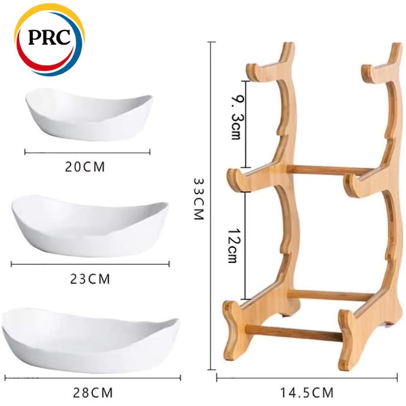 May include: Three white oval ceramic bowls measuring 20 cm, 23 cm, and 28 cm in width, accompanied by a light brown wooden tiered display stand. The stand features two levels with a total height of 33 cm, a width of 14.5 cm, and tier gaps of 9.3 cm and 12 cm.