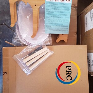 May include: A bamboo cat-shaped stand kit featuring two light-colored wooden side panels, three cylindrical wooden dowels, a small screwdriver, and an instruction sheet with diagrams, all packaged in plastic and cardboard for assembly.