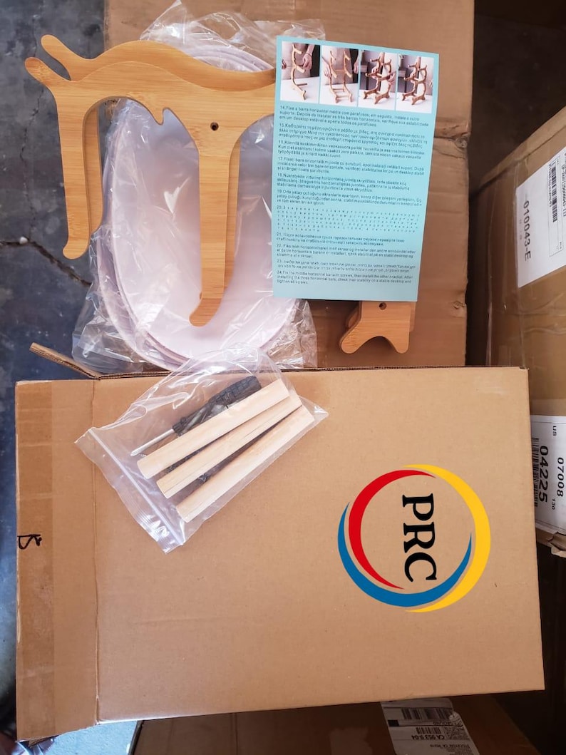 May include: A bamboo cat-shaped stand kit featuring two light-colored wooden side panels, three cylindrical wooden dowels, a small screwdriver, and an instruction sheet with diagrams, all packaged in plastic and cardboard for assembly.