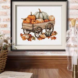 Könnte beinhalten: Ein gerahmtes Kreuzstichbild, das einen hölzernen Leiterwagen zeigt, der mit verschiedenen Kürbissen in Orange-, Grün- und Weißtönen beladen ist. Der Wagen steht auf einem Haufen herbstlicher Blätter, umgeben von weiteren Kürbissen am Boden.