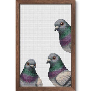 May include: A framed cross-stitch artwork featuring three pigeons. The birds have gray, green, and purple plumage, with orange eyes. The artwork is set against a white background and framed in a brown wooden frame.
