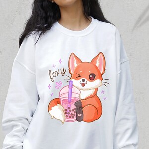 May include: White sweatshirt with a cartoon fox holding a pink boba tea cup. The fox is winking and the text "foxy" is above the fox.