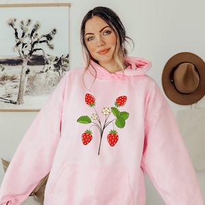 May include: A pink hoodie with a graphic of a strawberry plant with five strawberries and white flowers.
