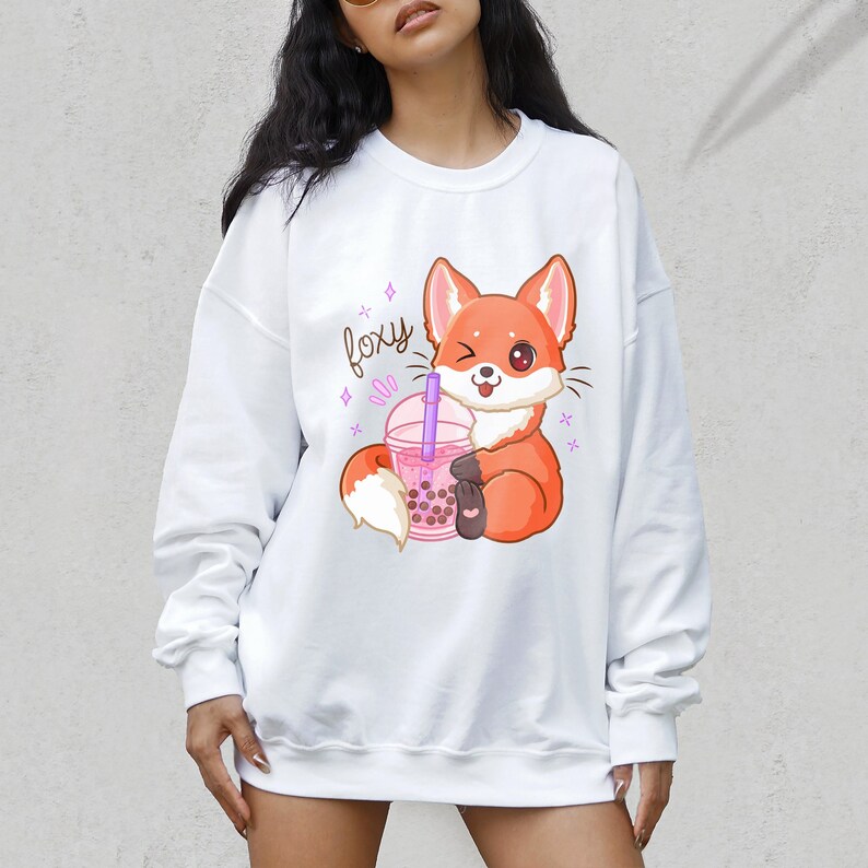 May include: White sweatshirt with a cartoon fox holding a pink boba tea cup. The fox is winking and the text "foxy" is above the fox.