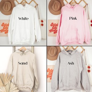 May include: Four hooded sweatshirts in different colours: white, pink, sand, and ash. Each sweatshirt has a simple, black text design on the front, reading "White", "Pink", "Sand", and "Ash" respectively.
