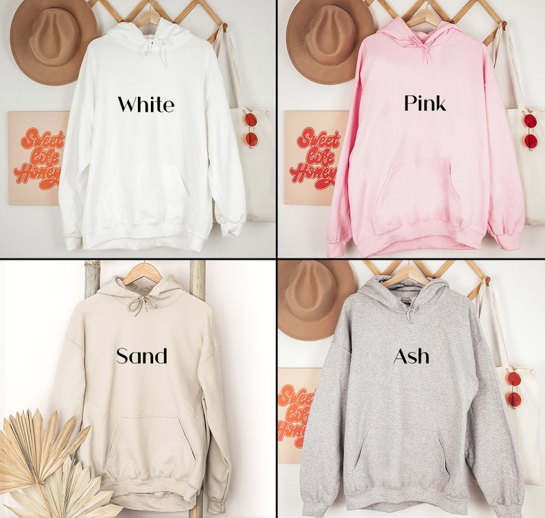 May include: Four hooded sweatshirts in different colours: white, pink, sand, and ash. Each sweatshirt has a simple, black text design on the front, reading "White", "Pink", "Sand", and "Ash" respectively.