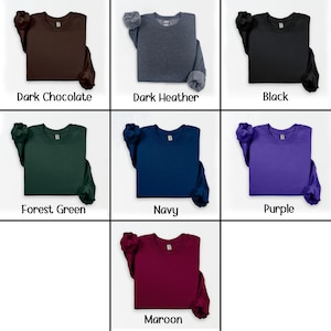 Pu&ograve; includere: Una collezione di felpe girocollo in vari colori tinta unita, tra cui cioccolato fondente, grigio scuro, nero, verde foresta, blu navy, viola e bordeaux. Ogni felpa &egrave; esposta con il nome del colore sottostante.