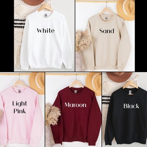 May include: Five crewneck sweatshirts in different colors: white, sand, light pink, maroon, and black. Each sweatshirt has a simple, bold text design on the front. The text reads "White", "Sand", "Light Pink", "Maroon", and "Black".