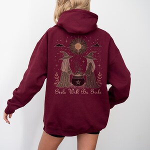 Pu&ograve; includere: Felpa con cappuccio bordeaux con una grafica di due streghe, un calderone, un sole e la scritta "Girls Will Be Girls". Il design &egrave; in oro e marrone. La felpa ha un cappuccio e maniche lunghe.