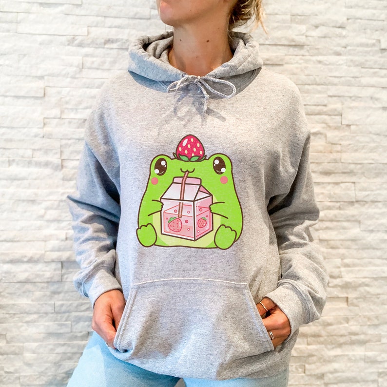 May include: A grey hooded sweatshirt featuring a cartoon frog wearing a strawberry on its head and drinking strawberry milk from a carton.