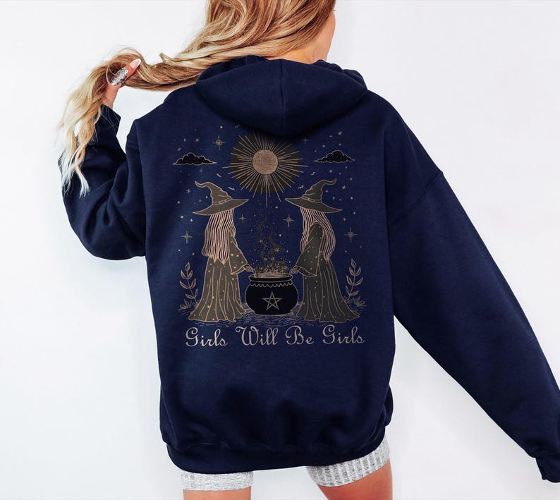 Pu&ograve; includere: Felpa con cappuccio blu navy con una grafica sul retro raffigurante due streghe, un calderone e la scritta "Girls Will Be Girls". Il design include un sole, stelle ed elementi decorativi. La felpa ha un cappuccio e maniche lunghe.