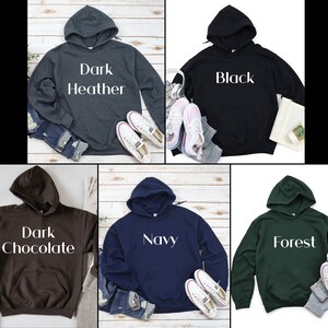 Puede incluir: Cinco sudaderas con capucha en diferentes colores: gris oscuro jaspeado, negro, chocolate oscuro, azul marino y verde bosque. Cada sudadera tiene una etiqueta de texto blanco en la parte delantera con el nombre del color.