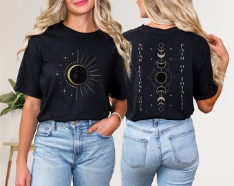Puede incluir: Camiseta negra con un gráfico dorado de una luna creciente y el sol con estrellas en la parte delantera. La parte posterior de la camiseta tiene un gráfico dorado de una luna creciente, el sol y estrellas con el texto "Solar Eclipse 2024 Path of Totality".