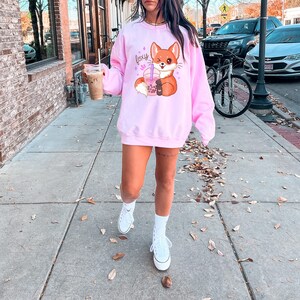 May include: Pink sweatshirt with a cartoon fox holding a boba tea and the word "foxy" in pink glitter letters.