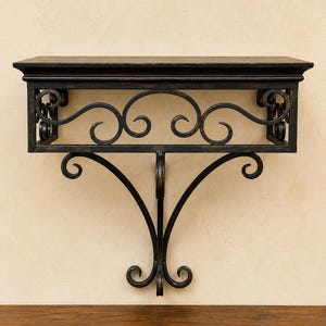 May include: A wall-mounted console shelf featuring a flat rectangular top and a black metal frame. The frame is decorated with intricate scrollwork and curved metal supports that extend downward, creating a decorative openwork design.