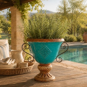 May include: A turquoise ceramic urn planter with a wide rim and a pedestal base. The planter features two black metal scroll handles on the sides and a square embossed floral design on the front. It is filled with a lush green rosemary plant.