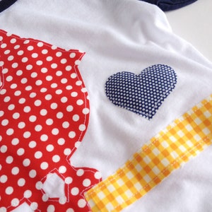 May include: White t-shirt with a red and white polka dot design, a blue heart with white polka dots, and a yellow and white checkered ribbon.