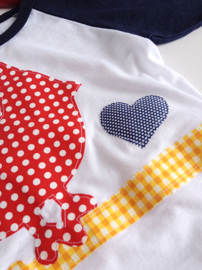 May include: White t-shirt with a red and white polka dot design, a blue heart with white polka dots, and a yellow and white checkered ribbon.
