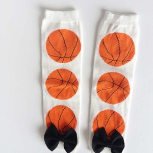 Puede incluir: Un par de calentadores de piernas blancos con un patr&oacute;n de baloncesto y lazos negros en la parte inferior.