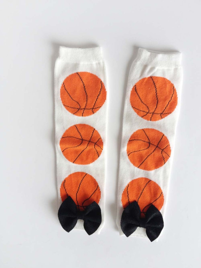 Puede incluir: Un par de calentadores de piernas blancos con un patr&oacute;n de baloncesto y lazos negros en la parte inferior.