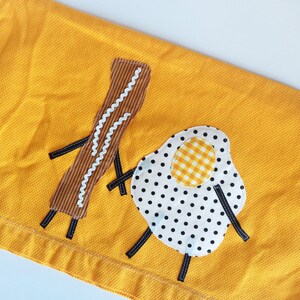 Puede incluir: Una toalla de cocina amarilla con un dise&ntilde;o bordado de un huevo frito y una loncha de tocino.