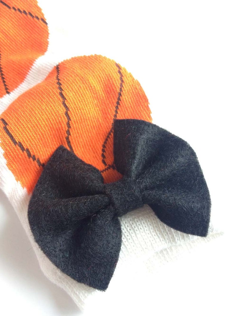 Puede incluir: Un lazo de terciopelo negro atado en un par de calcetines blancos con dise&ntilde;os de baloncesto naranja.