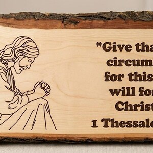 Puede incluir: Placa de madera con borde natural, con una imagen grabada de Jesús y el versículo bíblico "Dad gracias en todo, porque esta es la voluntad de Dios para vosotros en Cristo Jesús 1 Tesalonicenses 5:18".
