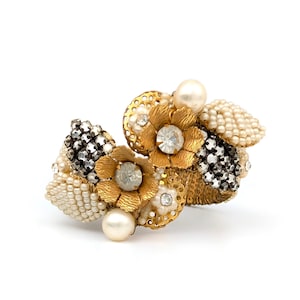 May include: A vintage floral brooch featuring gold-tone metal flowers with clear rhinestone centers, surrounded by cream-colored and black beaded accents, and faux pearls. The brooch is a unique piece of jewelry.