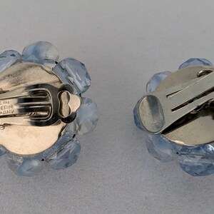 May include: A pair of vintage clip-on earrings. Each earring features a cluster of light blue faceted beads surrounding a silver-tone metal backing. The clip mechanism is visible, and the earrings are marked "MADE IN WESTERN GERMANY".