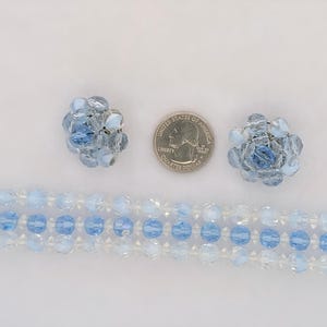 May include: A vintage jewelry set featuring a bracelet and matching clip-on earrings. The bracelet is made of light blue and clear beads, with a silver-tone clasp. The earrings are floral-shaped, also with light blue beads.