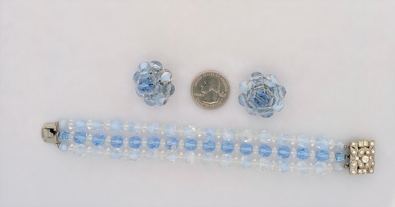 May include: A vintage jewelry set featuring a bracelet and matching clip-on earrings. The bracelet is made of light blue and clear beads, with a silver-tone clasp. The earrings are floral-shaped, also with light blue beads.