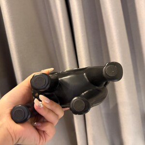 May include: A black ceramic bulldog figurine with four round feet. The figurine is glossy and appears to be a decorative item. The bulldog is seen from the underside, with its feet facing the viewer.