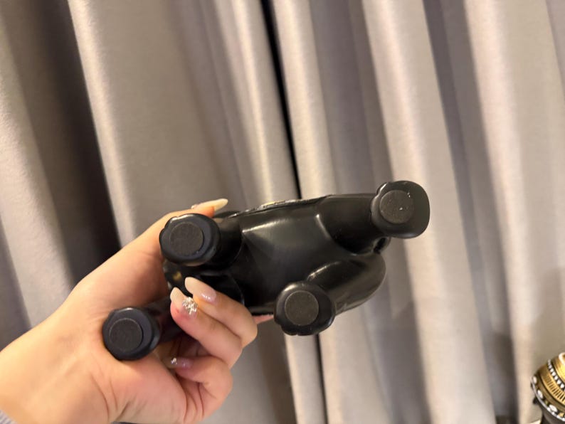 May include: A black ceramic bulldog figurine with four round feet. The figurine is glossy and appears to be a decorative item. The bulldog is seen from the underside, with its feet facing the viewer.